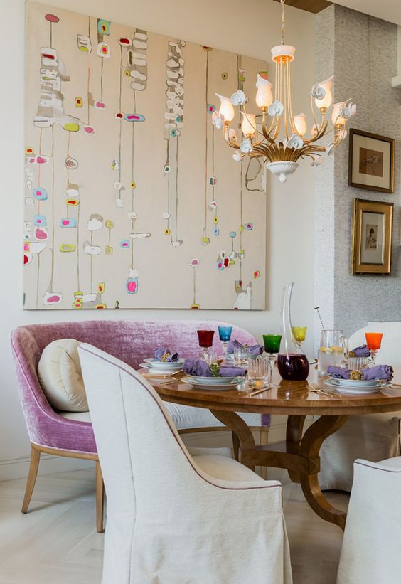 a bright eclectic dining room with a stained table, a lilac loveseat, neutral antique chairs and a bold artwork