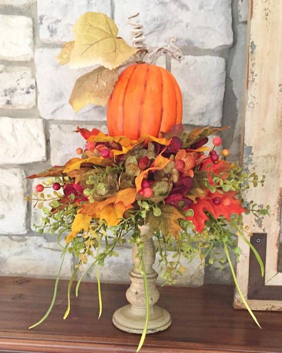 a bright faux pumpkin with lots of faux leaves, greenery and berries placed on a wooden stand