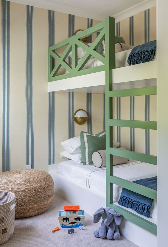 a bright kids' room with striped walls, a green bunk bed, neutral and navy bedding, a jute pouf, a basket and toys