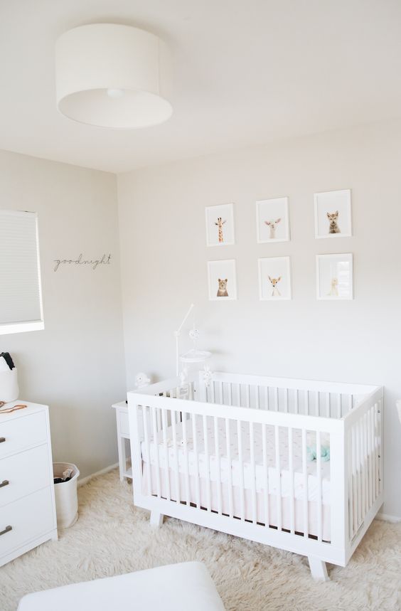 a calming neutral nursery with a gallery wall of animal portraits, a white IKEA Sundvik crib, a faux fur rug and some whites and off-whites
