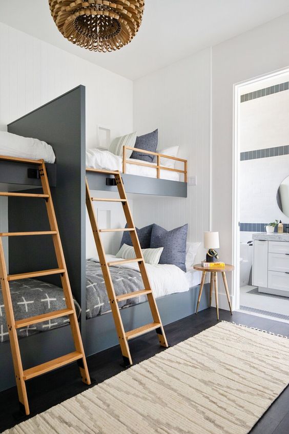 a catchy and contrasting graphite grey and white kids' room with four built-in bunk beds, wooden ladders and a side table, a wooden pendant lamp