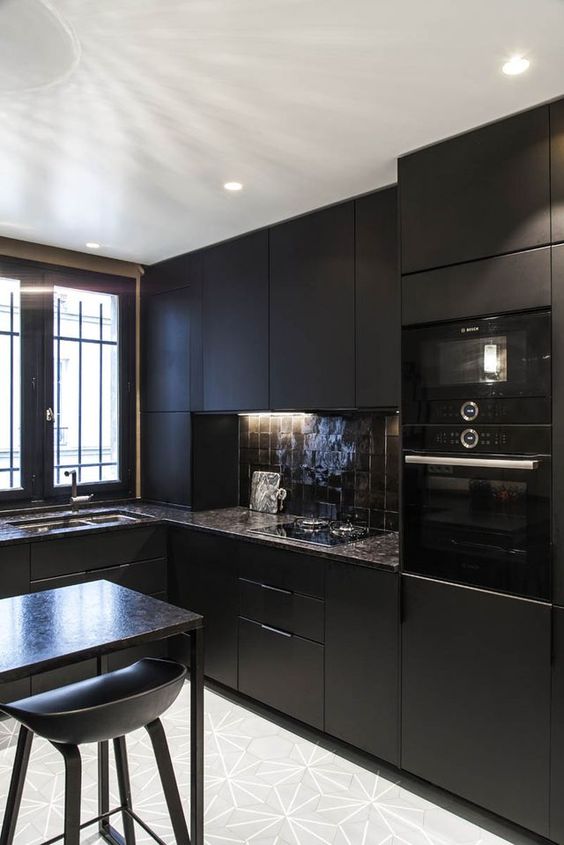 a chic black kitchen with a brown tile backsplash and brown stone countertops, a tall console table and stools