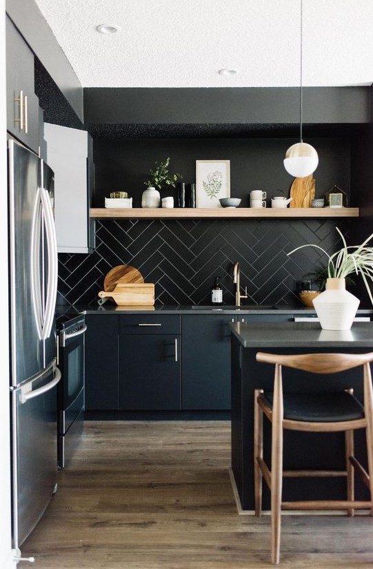 a chic black kitchen with black cabinets, a tile backsplash, concrete countertops and touches of light-colored wood