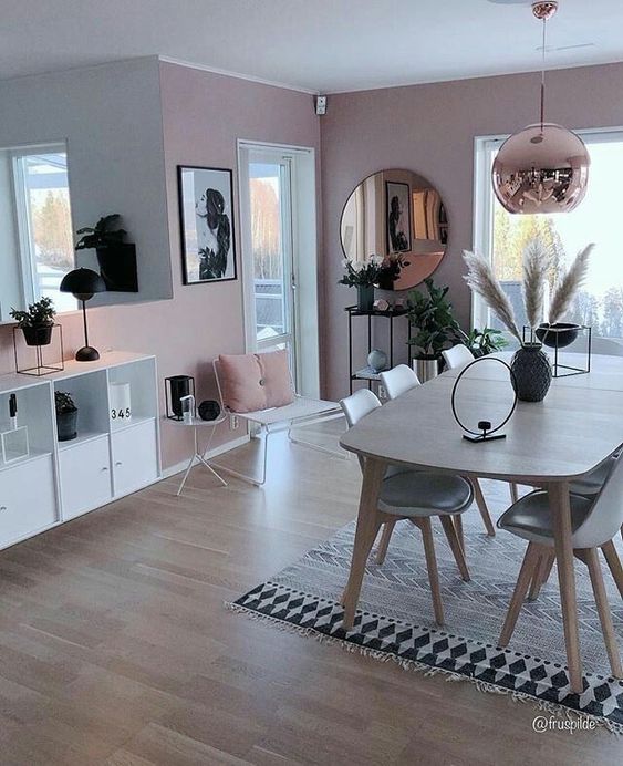 a chic dining space with pink walls, a stained table, grey chairs, a copper lamp and pink pillows