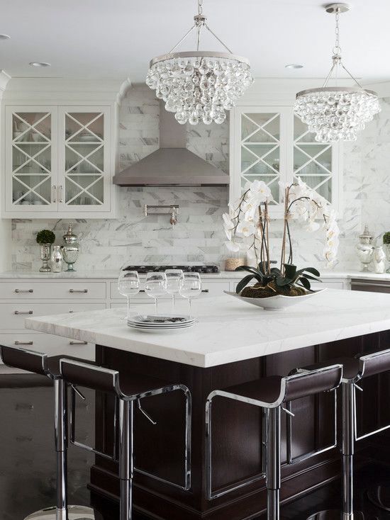 a chic glam kitchen with white cabinets and a chocolate brown kitchen island, crystal chandeliers, elegant curved stools