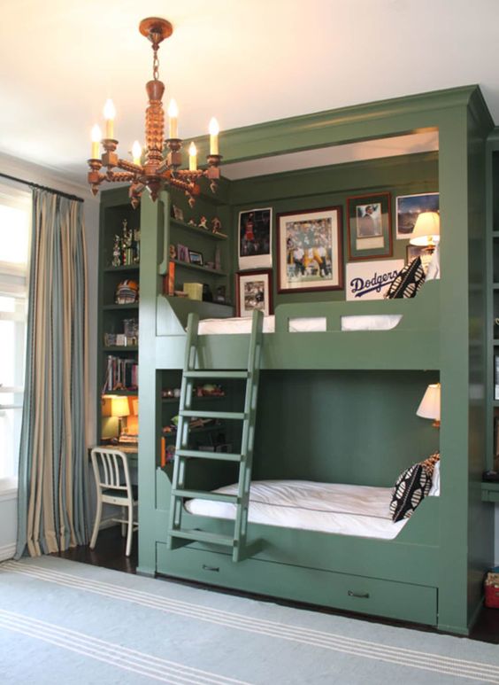a chic kids' room with green walls and a built in bunk bed, a ladder, a vintage chandelier and a built in desk space with shelves