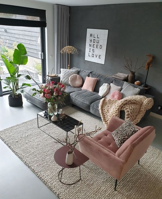 a chic living room with a graphite grey accent wall and a sofa, a pink chair, a black coffee table and a burgundy side table