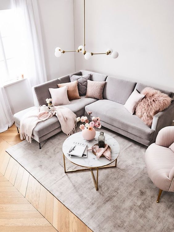 a chic living room with a grey sectional, pink pillows and a pink chair, a grey rug and a round table is a stylish space
