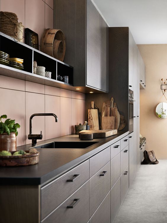 a chic modern kitchen with grey cabinetry and black countertops, a matte pink tile backsplash and black fixtures
