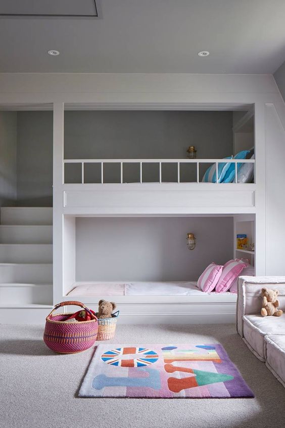 a clean minimal kids' room with built-in bunk beds, bright bedding and a rug, a low seat sofa by the window, baskets for storage and built-in lights