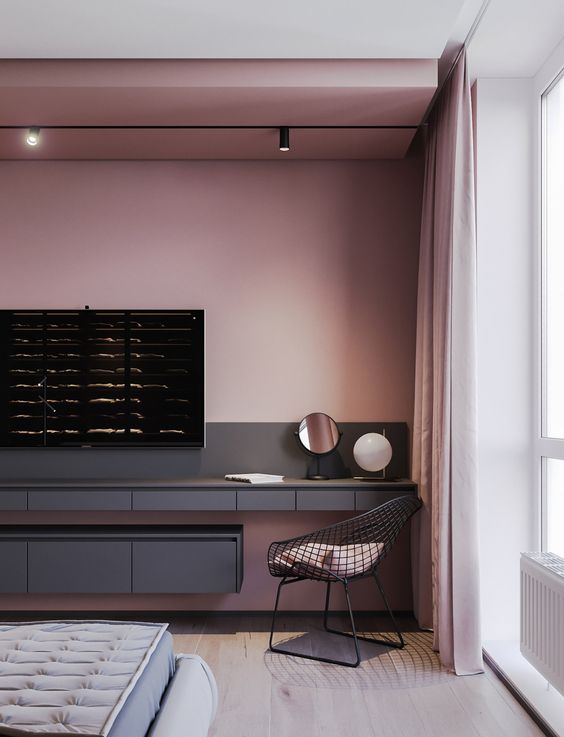 a contemporary bedroom with a pink accent wall, a black TV unit, a black chair, a grey bed with a grey mattress