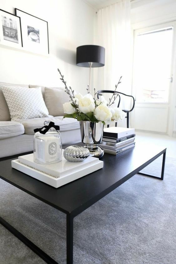 a contemporary black table with stacks of books, a metallic vase with white blooms and a candle