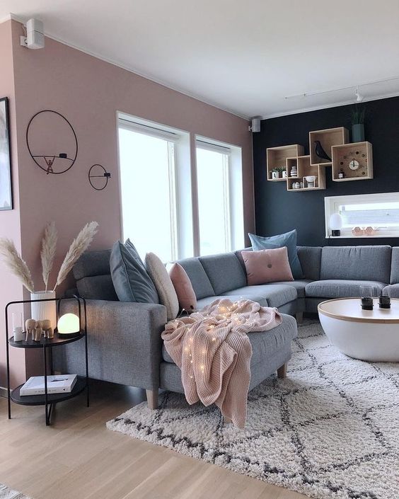 a contrasting living room with a pink and black wall, a grey sectional, a round table and box shelves plus pink pillows