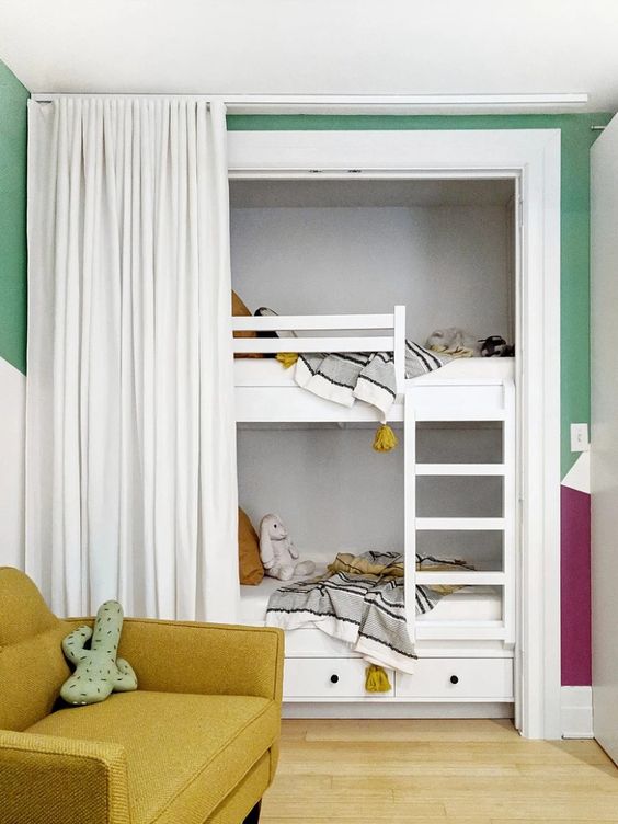 a cozy and bright kids' room with white built-in bunk beds, neutral bedding, a mustard chair and a curtain to get some privacy