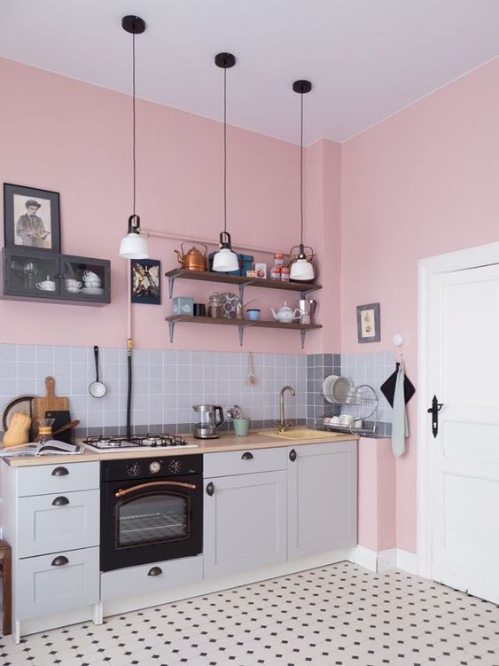 a cozy and lovely pink and grey kitchen with pink walls, a grey backsplash and cabinetry, a printed tile floor and pendant lamps