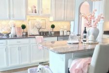 a cute glam kitchen with white cabinetry, stone countertops, a crystal chandelier, a lavender dog bed and touches of light pink