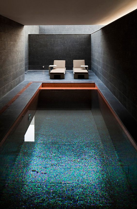 a dark pool house clad with graphite grey tiles, with a couple of loungers and a pool with very catchy mini tiles