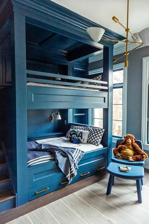 a deep blue kids' room with built-in bunk beds and navy and white bedding, with printed pillows and blankets, a chair and a footrest