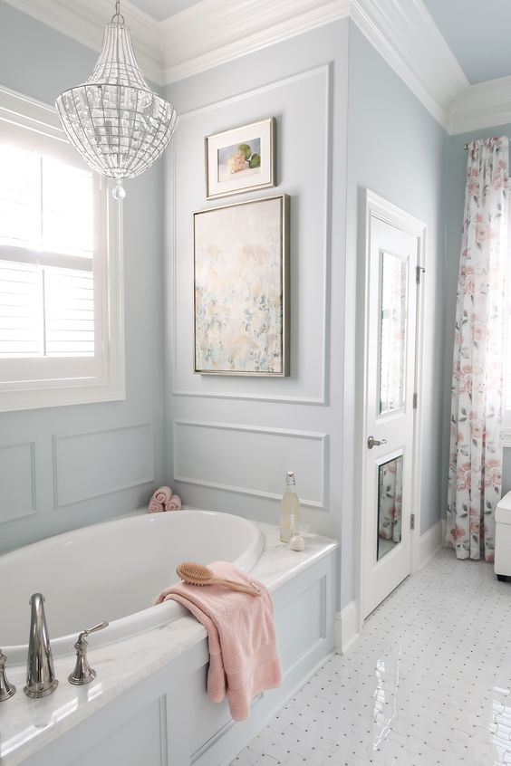 a dreamy pastel blue bathroom with molding, a bathtub with molding, too, a crystal chandelier and floral touches is pure chic