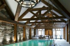 a fantastic pool house with an attic roof and wooden beams, a white sofa, a round chandelier, a large pool and a swing