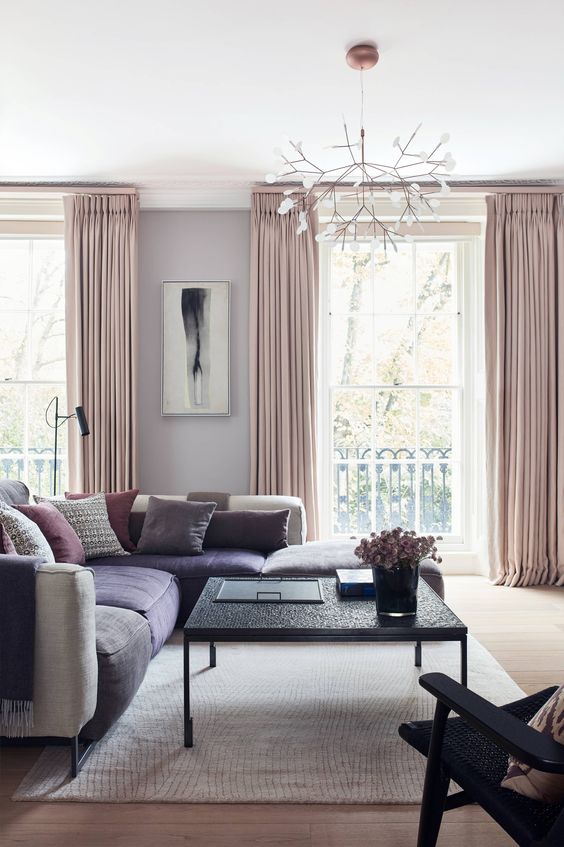 a glam living room with grey walls, a large grey and purple sectional, pink pillows and blush curtains