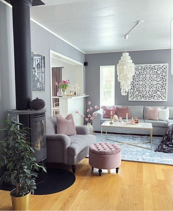 a glam living room with grey walls, grey sofas and a loveseats, pink pillows and a pouf and a large chandelier