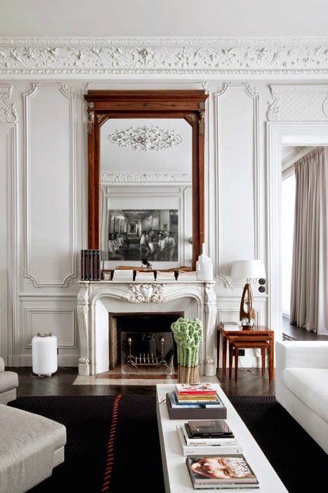 a gorgeous refined French interior with molding on the walls and ceiling, with a mirror in a stained frame, a vintage-inspired fireplace and white furniture