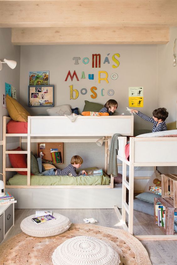 a grey kids' room with three bunk beds, ladders, a space for hanging out, crate bookshelves and bright decor