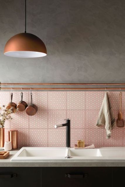 a grey kitchen with black cabinetry and a pink printed tile backsplash, a copper pendant lamp and copper pipes