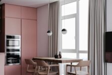 a laconic kitchen with grey walls and pink sleek cabinets, a stained table and chairs, black and white pendant lamps