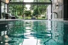 a large attic pool house with a glazed wall, some wicker furniture, a large pool with a faucet and a glazed wall to enjoy garden views