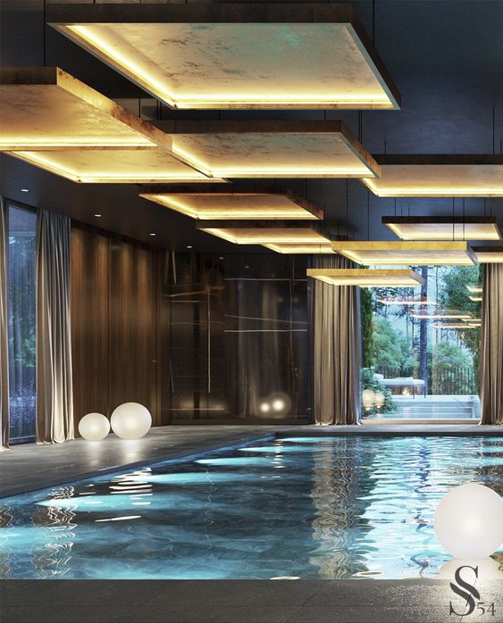 a large refined pool space with dark walls, a large pool and a stone deck, cool lights hanging over the pool and some float lights