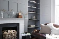a light-colored living room with grey walls and molding, a fireplace, niche walls and a brown leather sofa