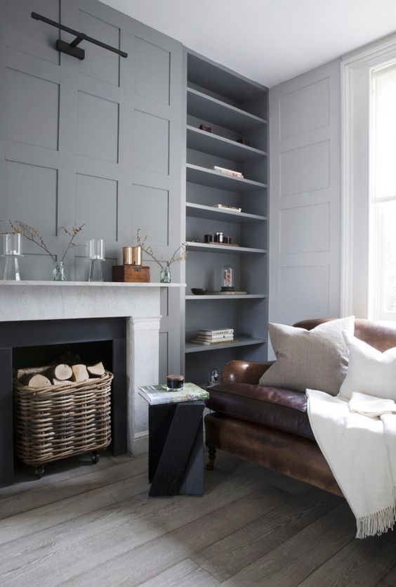 a light colored living room with grey walls and molding, a fireplace, niche walls and a brown leather sofa