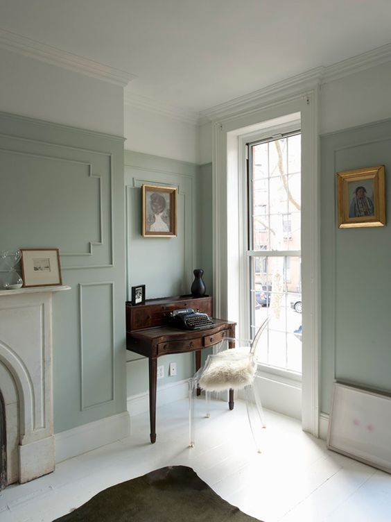 a light green living room with molding on the walls, neutral floors and a non-workign fireplace, artworks and refined vintage furniture