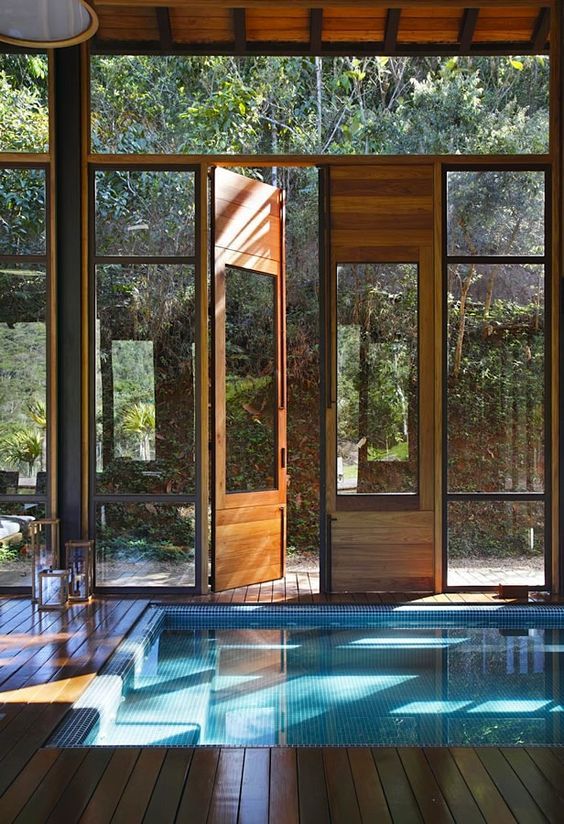 a lovely Japanese inspired pool house with glazed walls and doors and a lot of wood in decor, with a pool and natural light