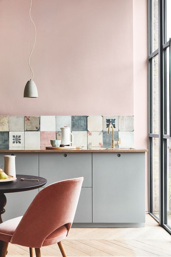 a lovely kitchen with pink walls, grey cabinets, a mismatching tile backsplash and pink chairs is super cool