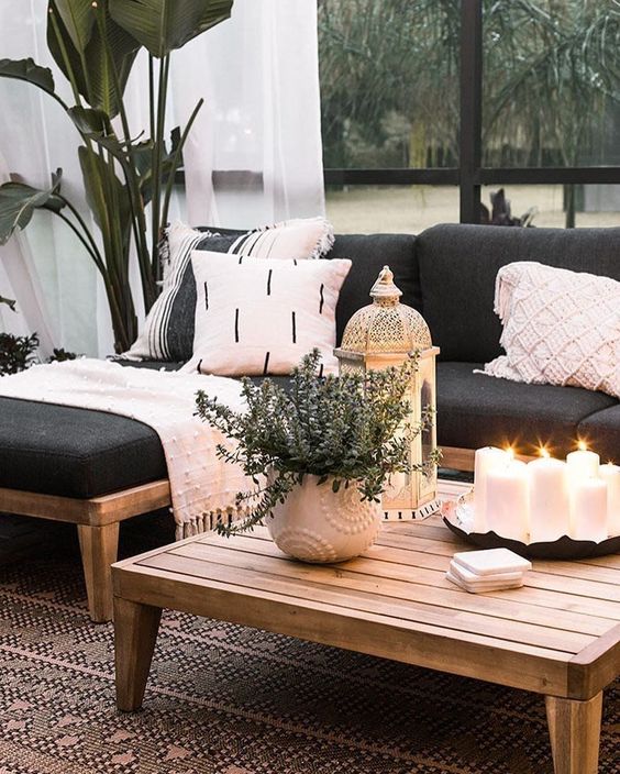 a low wooden coffee table with an arrangement of pillar candles in a tray, potted greenery and a candle lantern