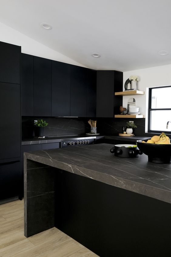 a matte black kitchen with a black marble backsplash and brown marble countertops, open shelves and some potted plants