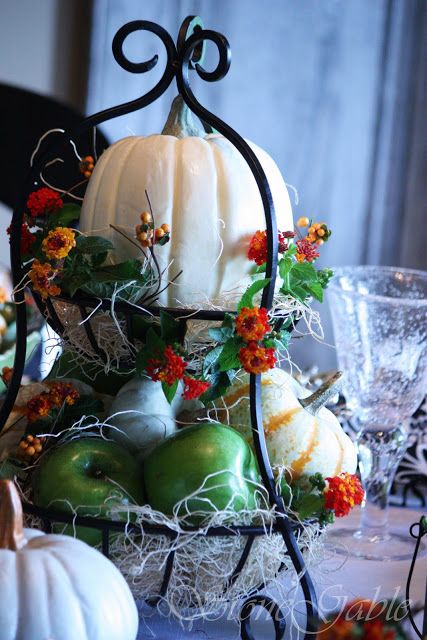 a metal tiered stand with hay, faux veggies and fruits and bright blooms plus large pumpkins for fall decor
