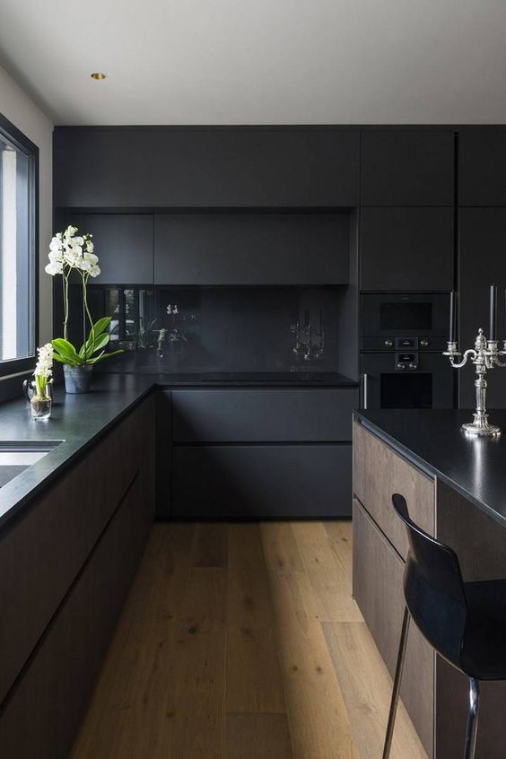 a minimalist black kitchen with matte cabinets, black countertops and a backsplash, a large kitchen island in black and with stain