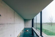 a minimalist pool house with concrete walls and a long and narrow pool plus a glazed wall that can be removed to make the space more outdoor