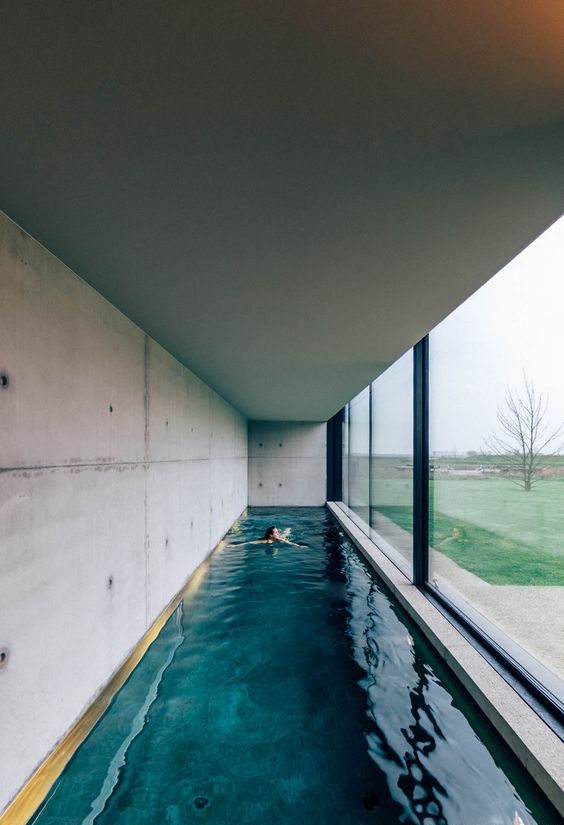 a minimalist pool house with concrete walls and a long and narrow pool plus a glazed wall that can be removed to make the space more outdoor