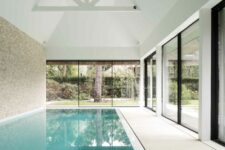 a minimalist pool house with glazed sliding doors and a large deep pool, the doors allow to make the pool both indoor and outdoor