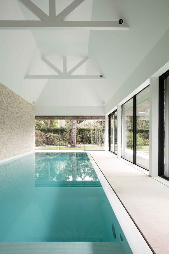 a minimalist pool house with glazed sliding doors and a large deep pool, the doors allow to make the pool both indoor and outdoor