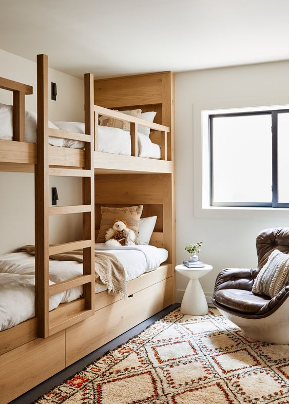 a modern and chic kids' space with stained wood bunk beds with a ladder, a leather chair, neutral bedding and a printed rug