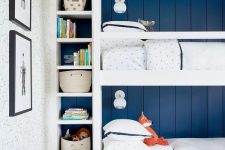 a modern and stylish kids’ room with navy shiplap walls, a white bunk bed built-in, built-in shelves, baskets, toys and artwork welcomes in