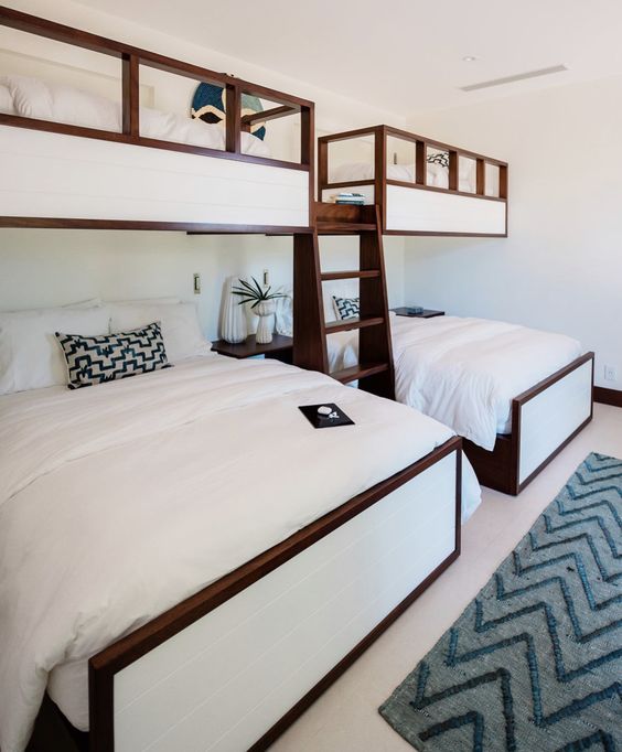 a modern boho kids' room with built-in bunk beds and neutral bedding, a grey printed rug, a dark-stained nightstand and potted plants