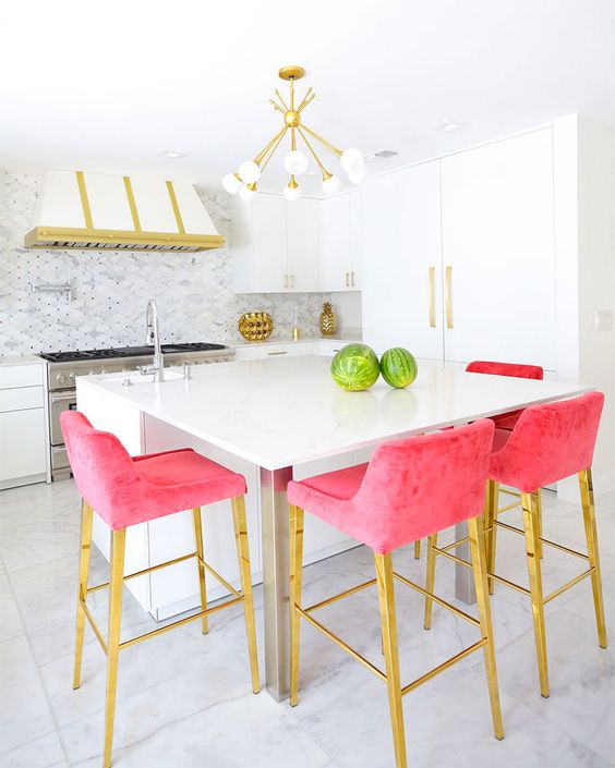 a modern glam kitchen with white cabinets, a white and gold hood, hot pink stools and a retro chandelier is wow