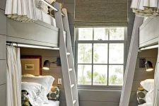 a modern grey kids’ room with built-in bunk beds, neutral and grey bedding, ladders and striped curtains plus black sconces